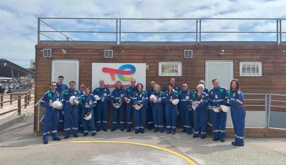Group of people in work clothes, posing in front of a prefabricated building - see detailed description hereafter
